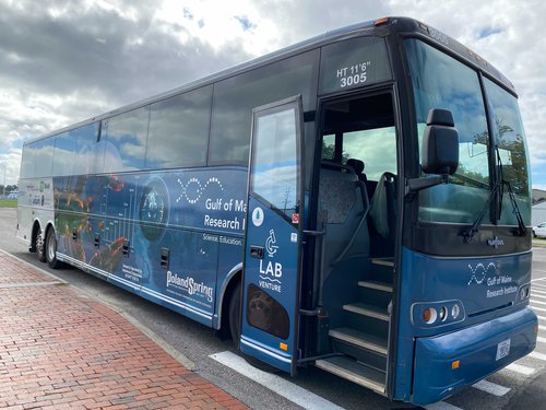 A blue, LabVenture decorated coach bus sits in a parking lot.