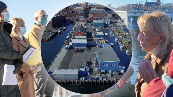 An aerial drone shot looking down on Union Wharf sits in a circle in the middle of the image. The image behind includes Governor Janet Mills speaking into a microphone on the right side of the image, and she's facing left.