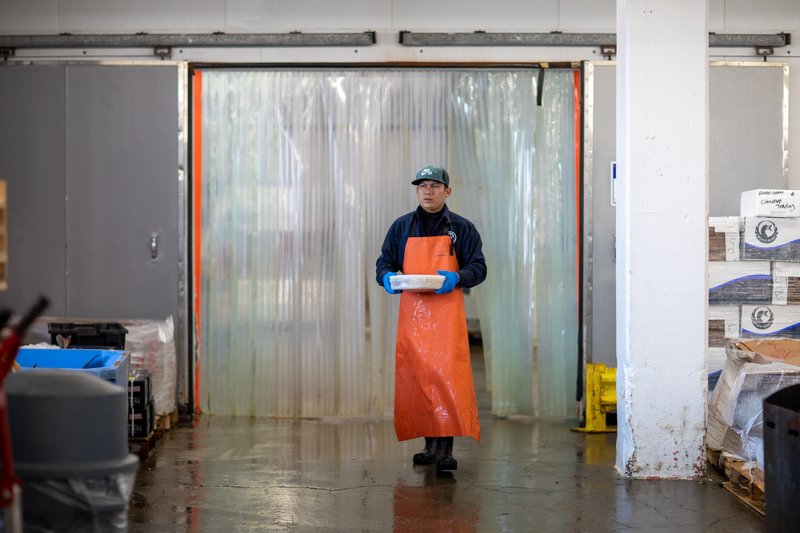 A worker at Red's Best seafood processing carrying some items in a plastic tub.