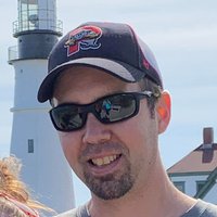 A portrait of a man with sunglasses and a baseball cap posing for the camera.