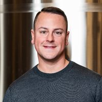 A portrait of a man smiling in a grey shirt.
