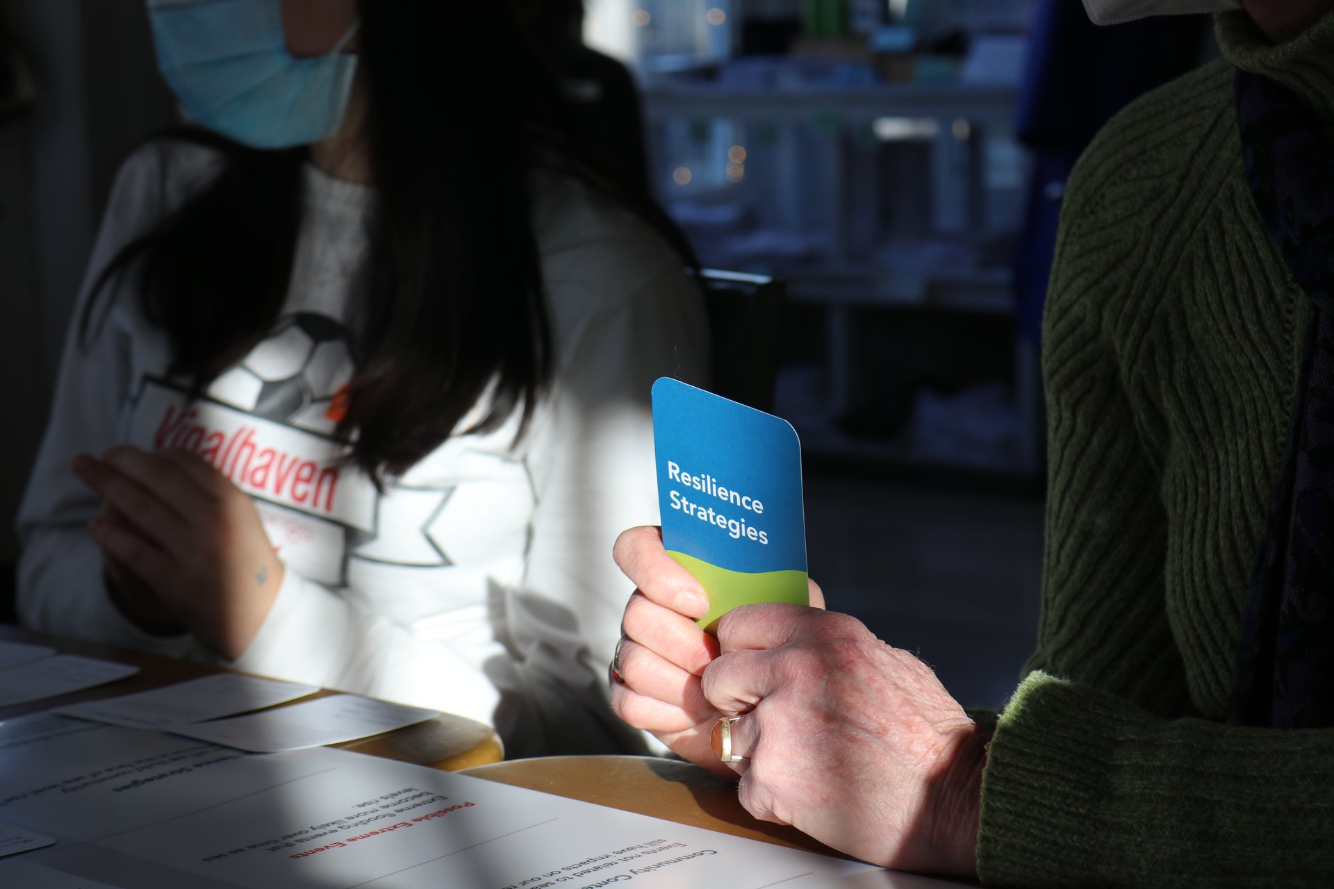 A woman is holding a blue and green card that reads "resilience strategies".
