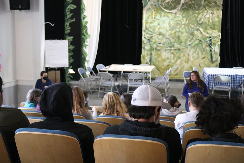 Students sit in an amphitheater, listening to someone speak.