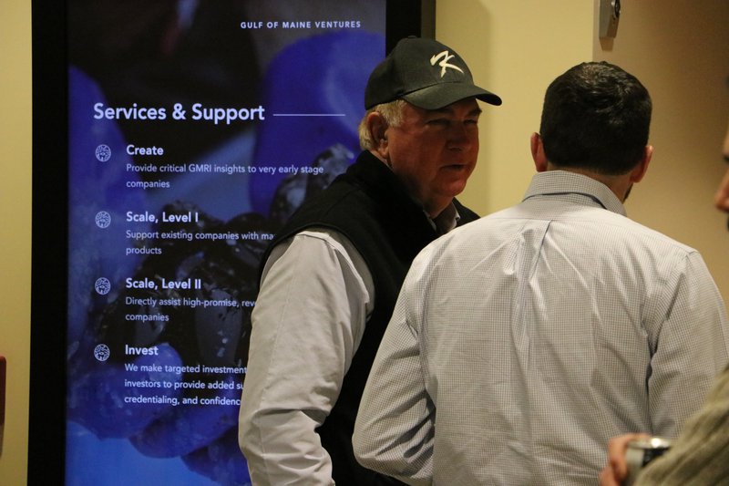 Two men are engaged in conversation in front of a virtual sign.