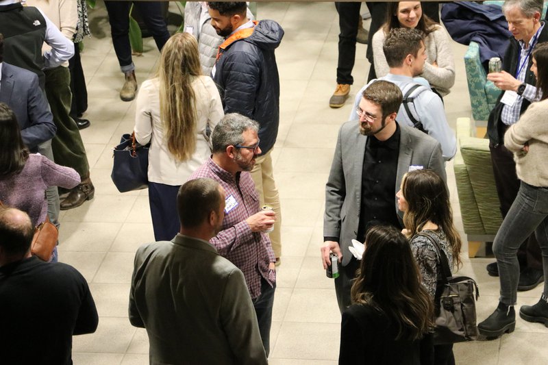 A large group of people are gathered in doors, engaged in coversation.
