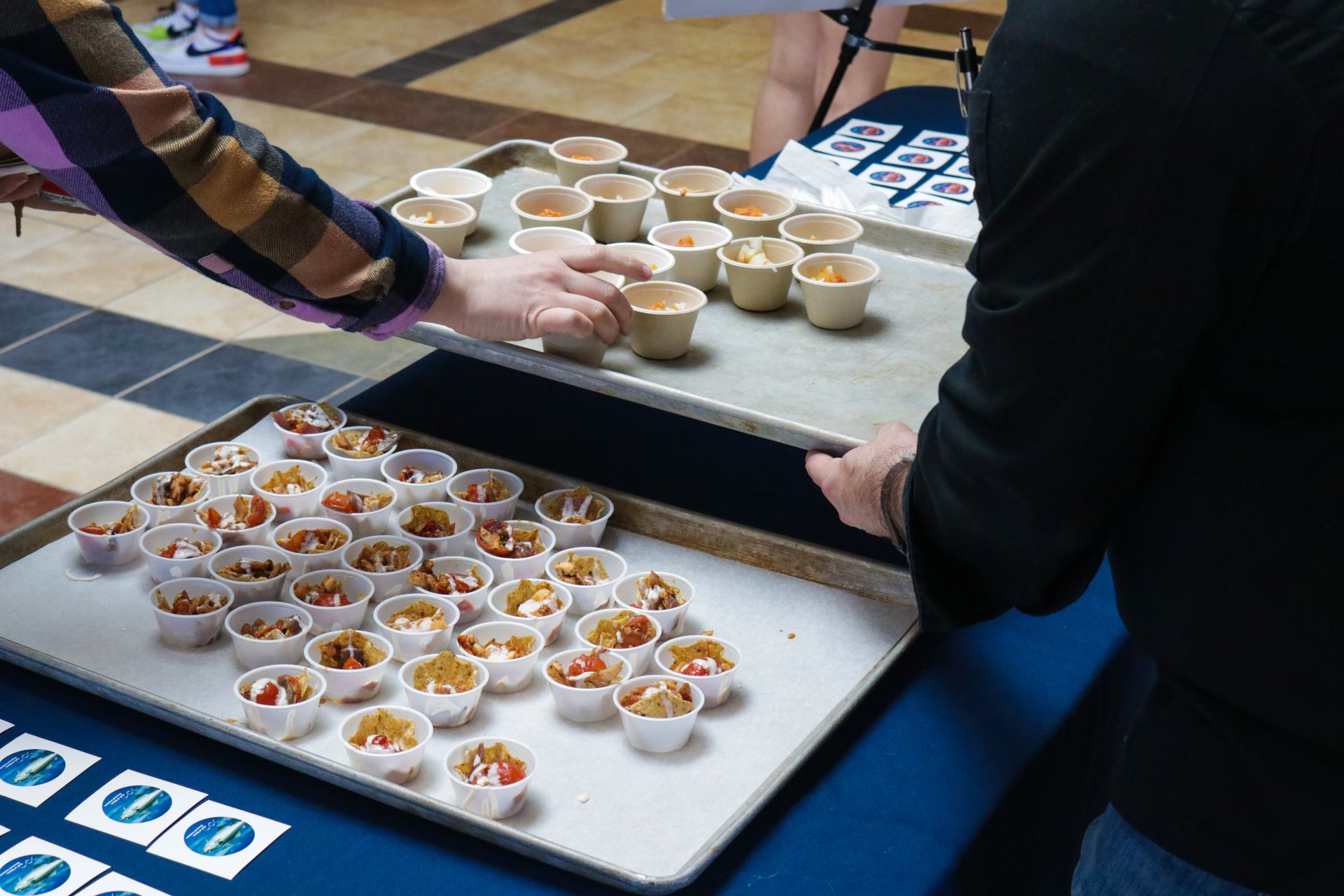 Seafood sits in cups on a desk. Hands reach for the delicious nuggets.