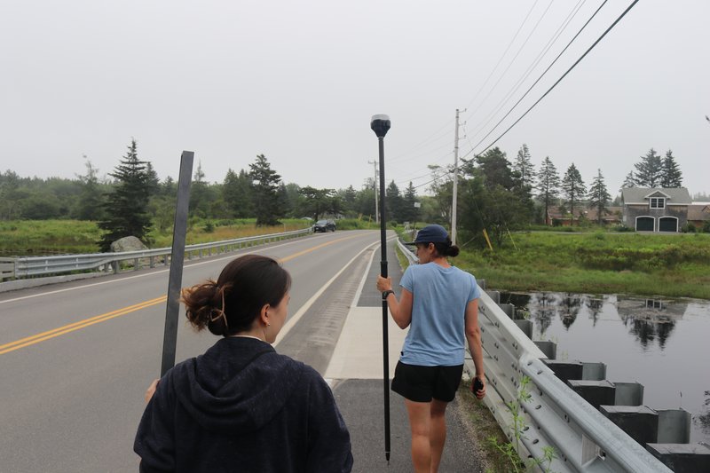 Two researchers walk on a bridge with elevation measuring tools.