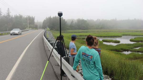 Four researchers stand at a roadside with an elevation measuring tool.