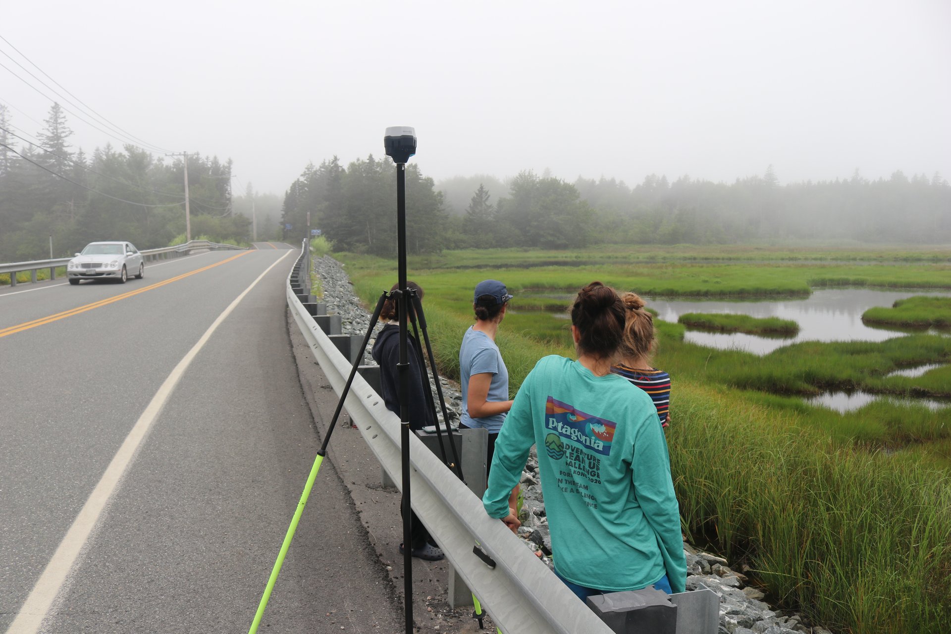 Four researchers stand at a roadside with an elevation measuring tool.