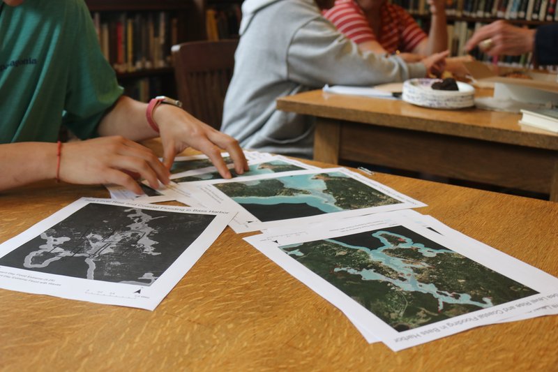 This photo shows maps scattered about on a wooden table.
