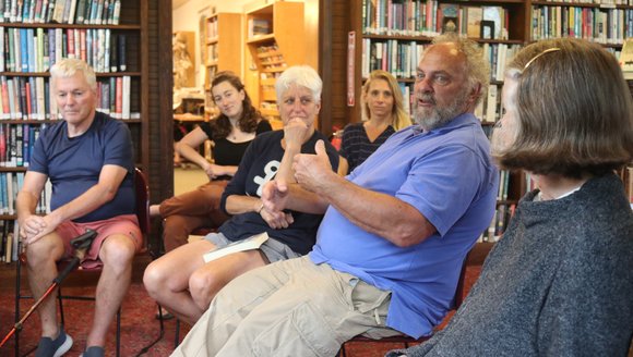People are gathered inside a small library in a discussion circle.