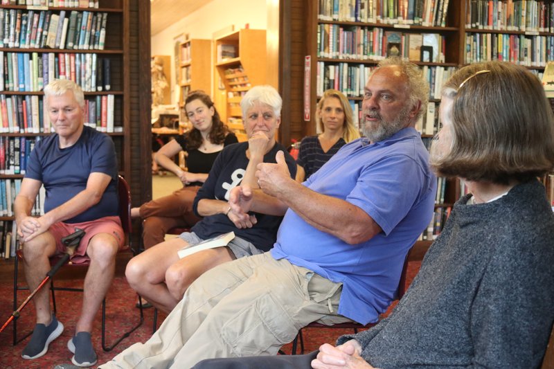 People are gathered inside a small library in a discussion circle.
