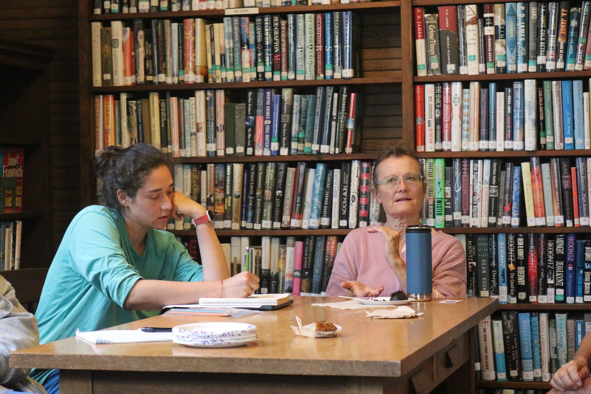 Two women are engaged in conversation inside a library.