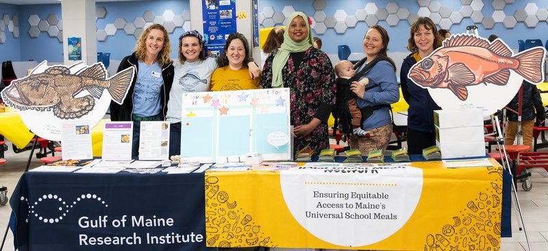 Seafood team staff members standing behind their table of seafood program information at a school.