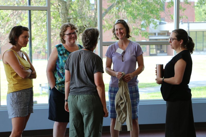 Five teachers gather in a circle indoors.