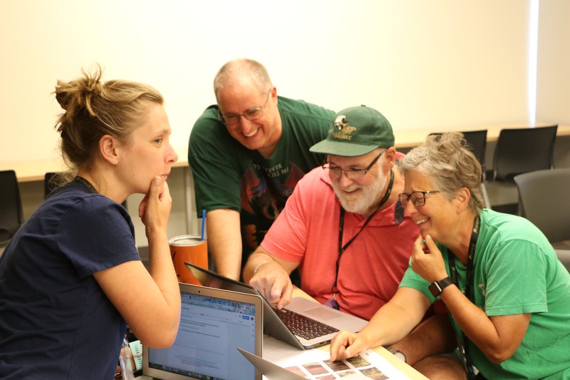 Teachers gather around a computer smiling at an RTC workshop.