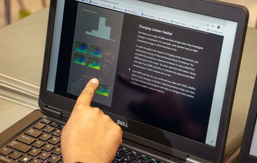 a middle school student pointing at a sea surface temperature map on a computer screen.