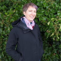 A woman with grey hair and a black coat smiles for the camera.
