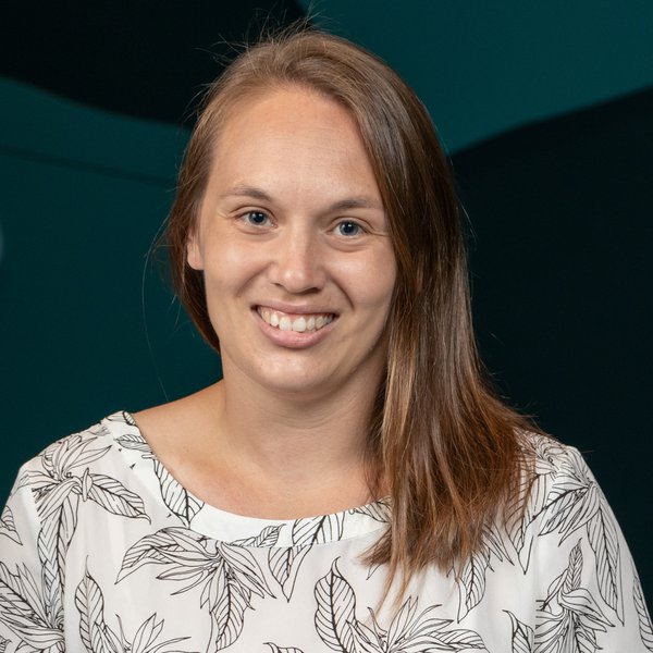 A woman smiles at the camera while standing in front of a wall with green and blue hues.