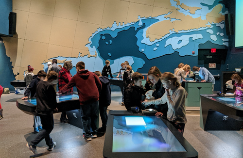 Students stand in groups at interactive learning tables inside the Cohen Center.