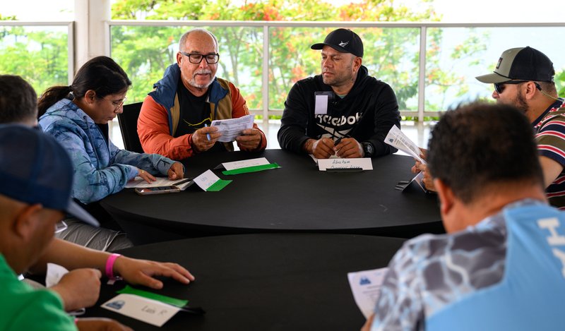 A group of fishermen sitting around a table discussing information in an MREP workshop.