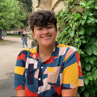 A person smiles for a portrait with short curly hair and a brightly colored button up shirt.