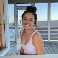 A portrait of a woman smiling in a pink tank top by a white table.