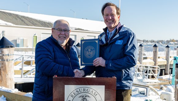 Glenn Prickett and Mayor Dion pose shaking hands and jointly holding the approved resolution.