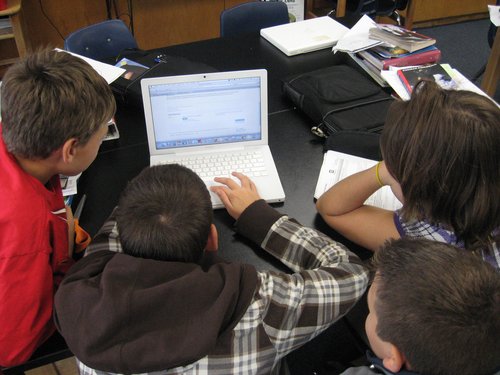 Students gather around a laptop.