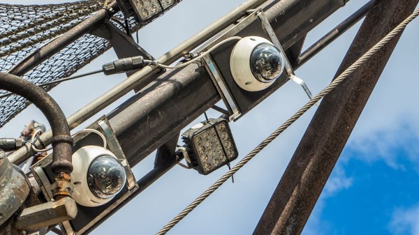 Two circular cameras with white bases and round lenses are mounted on a ship's beam that crosses the image frame diagonally from the bottom left of the image to the top right.