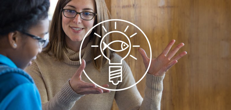 This is shows a white circle with a white outline of a lightbulb inside, centered in front of Sustainable Seafood Program Manager Kyle Foley in a brown shirt, engaging with a consumer.