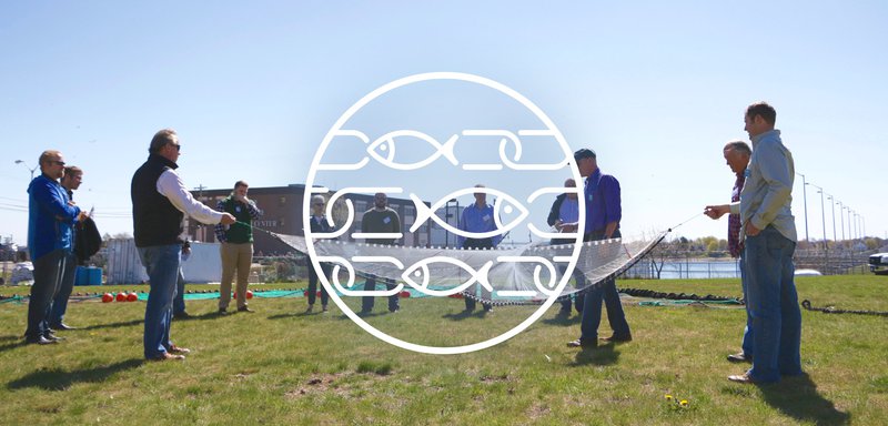 This image has a white circle with white fish drawn as links in chains inside, centered over a group of fishermen gathered outside holding a fishing net.