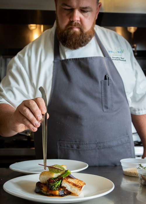 A chef placing a leaf on a seafood dish with tongs