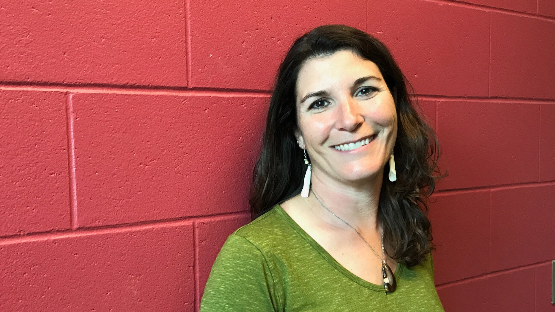 Gorham Middle School teacher and 2017 McCarthy Award winner Angela Gospodarek stands smiling in front of a red painted wall in a green blouse.