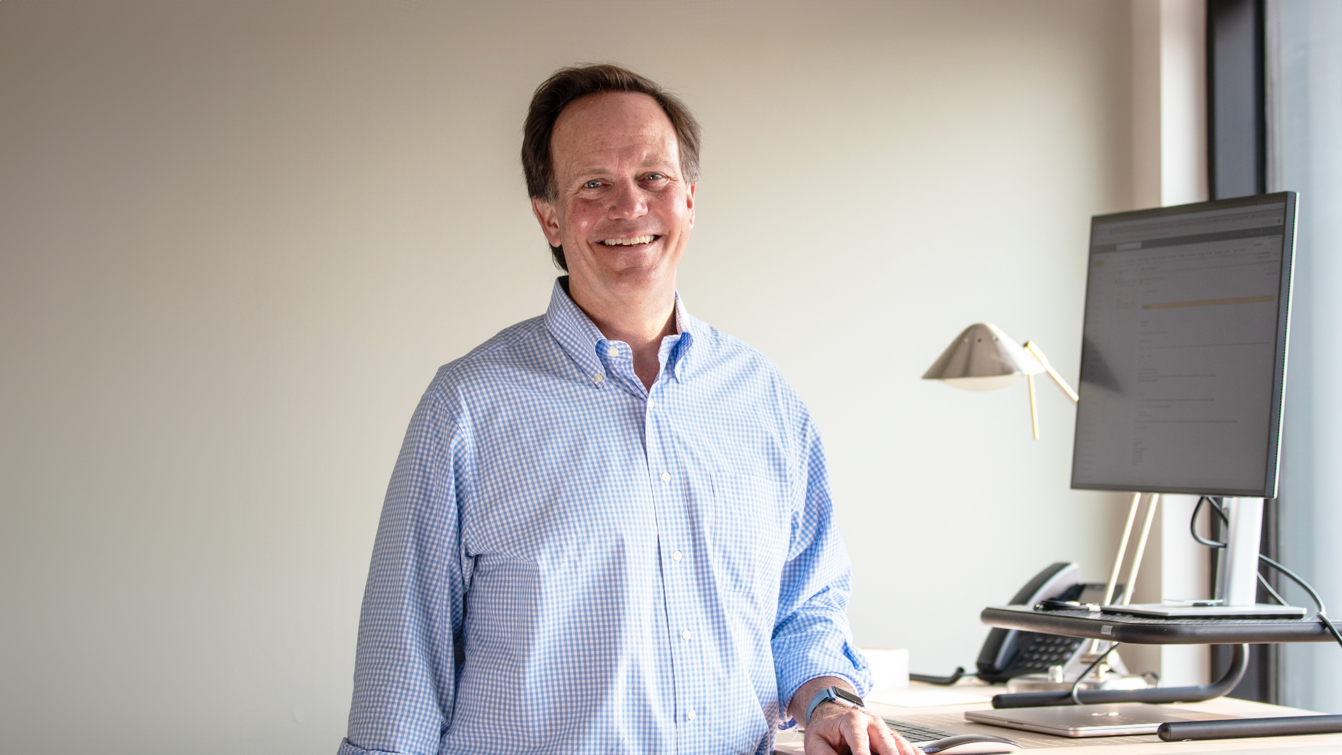 ceo glenn prickett standing at his desk and smiling