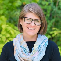 A portrait of a woman with glasses, a blue scarf, and a black shirt smiling for the camera.