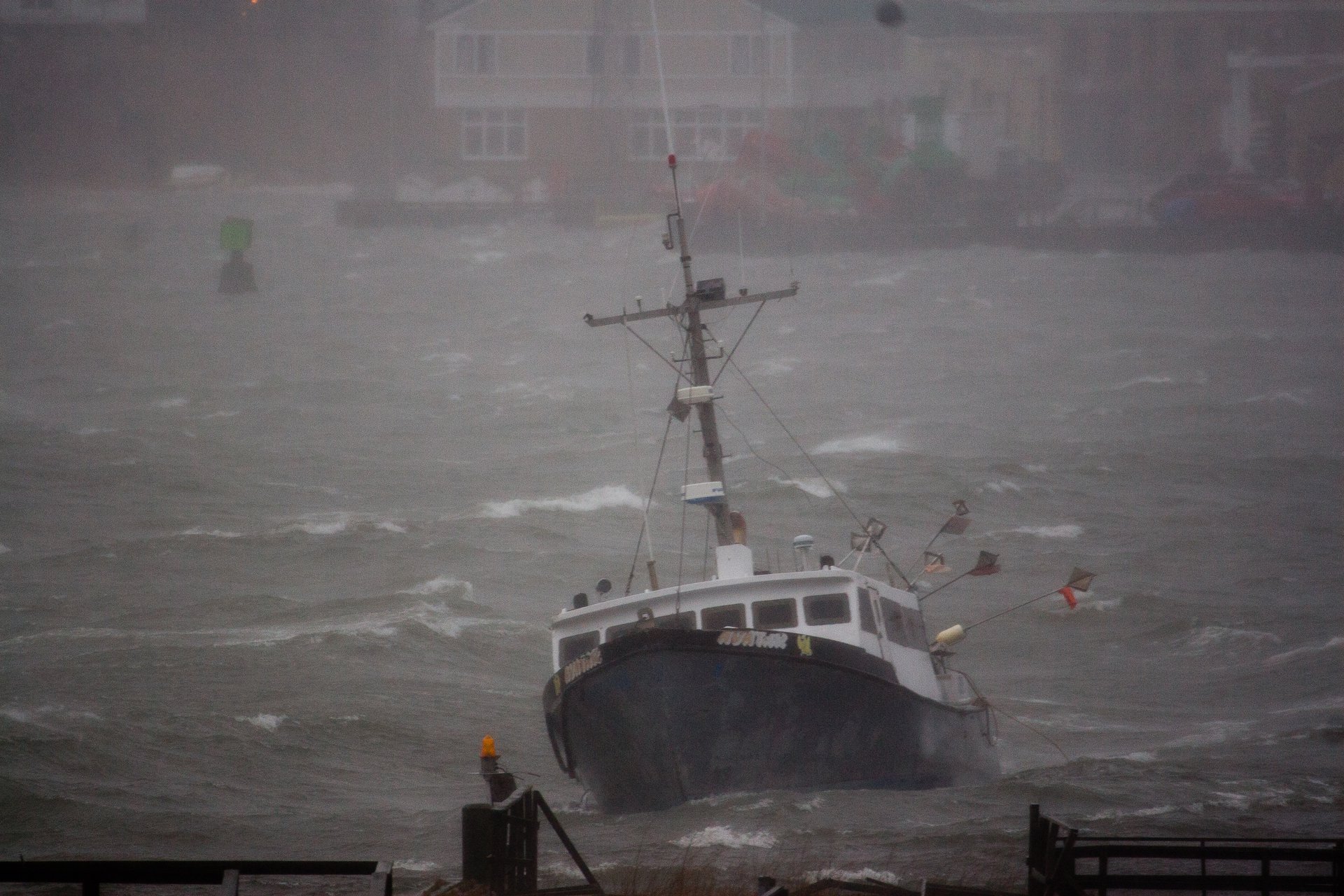 A blue and white boat lists to the starboard side in turbulent, stormy waters as rain pours.