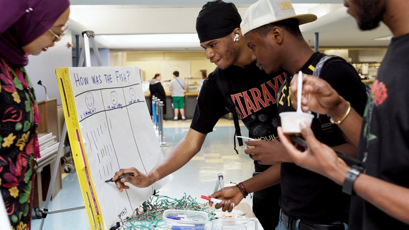 Three high school students marking a board, noting whether they liked or disliked the seafood sample.