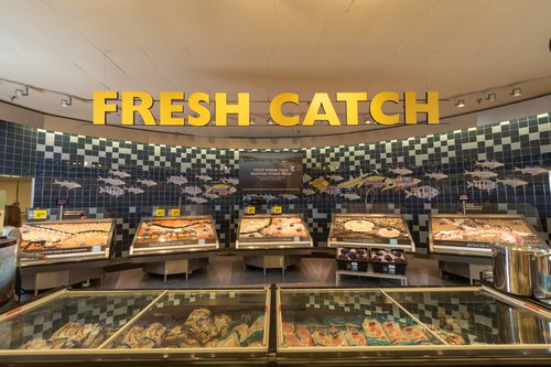 This is a photo inside a grocery store at the seafood counter. A sign reading "FRESH CATCH" sits above rows of fresh seafood.