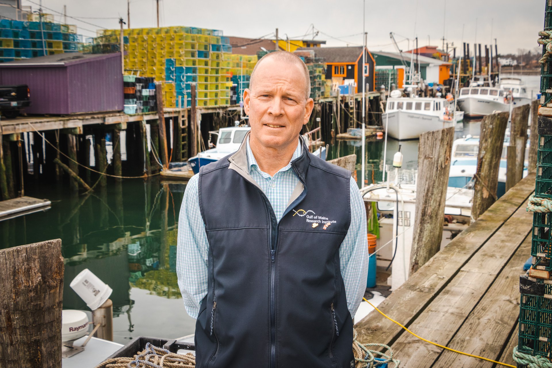 A man standing on a wharf with the ocean and fishing boats in the background.