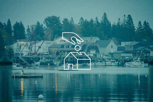 This is a white, line drawn graphic of a hand dropping a ball into the outline of a building, layered on top of a faded blue image of a working waterfront.