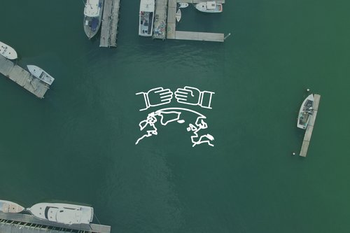 This is a white, line drawn graphic layered on top of an aerial shot looking straight down on a marina, scattered with boats and docks.